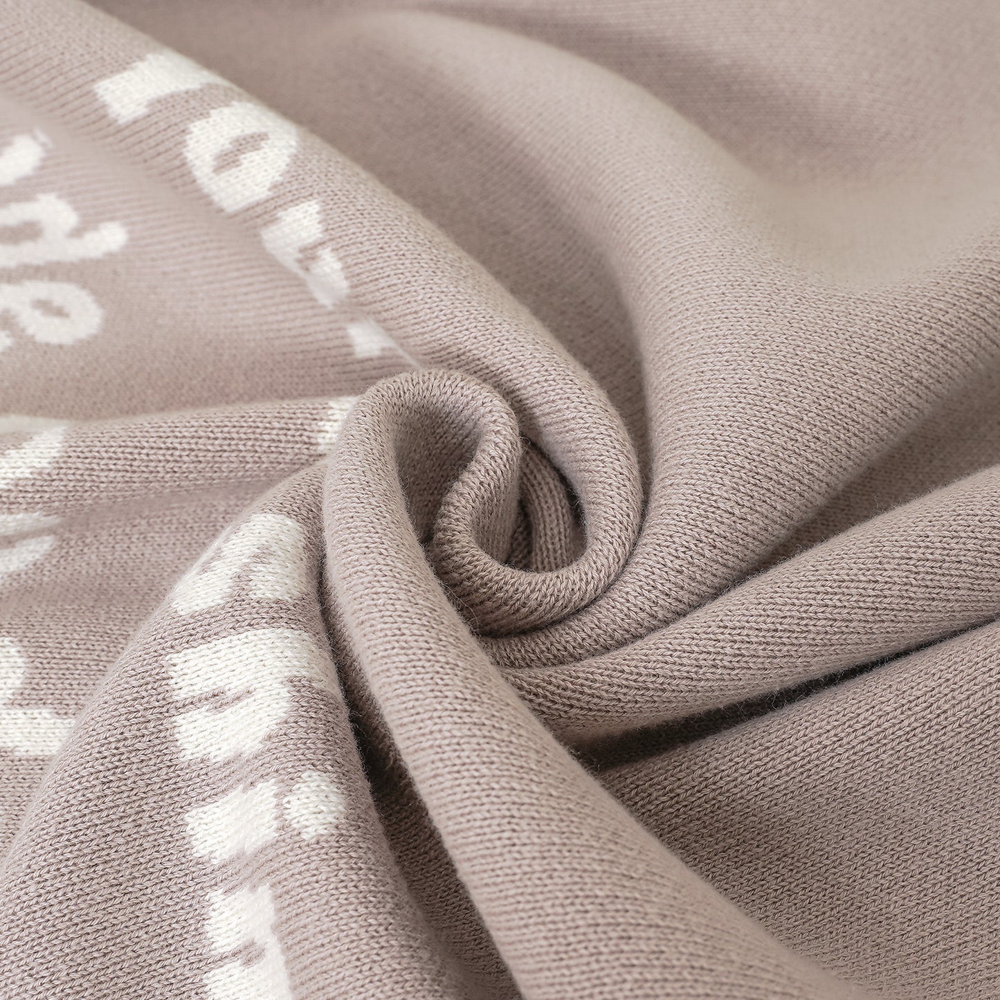 Close-up of a soft beige knit baby blanket, showing texture and white scripture text Luke 2:52