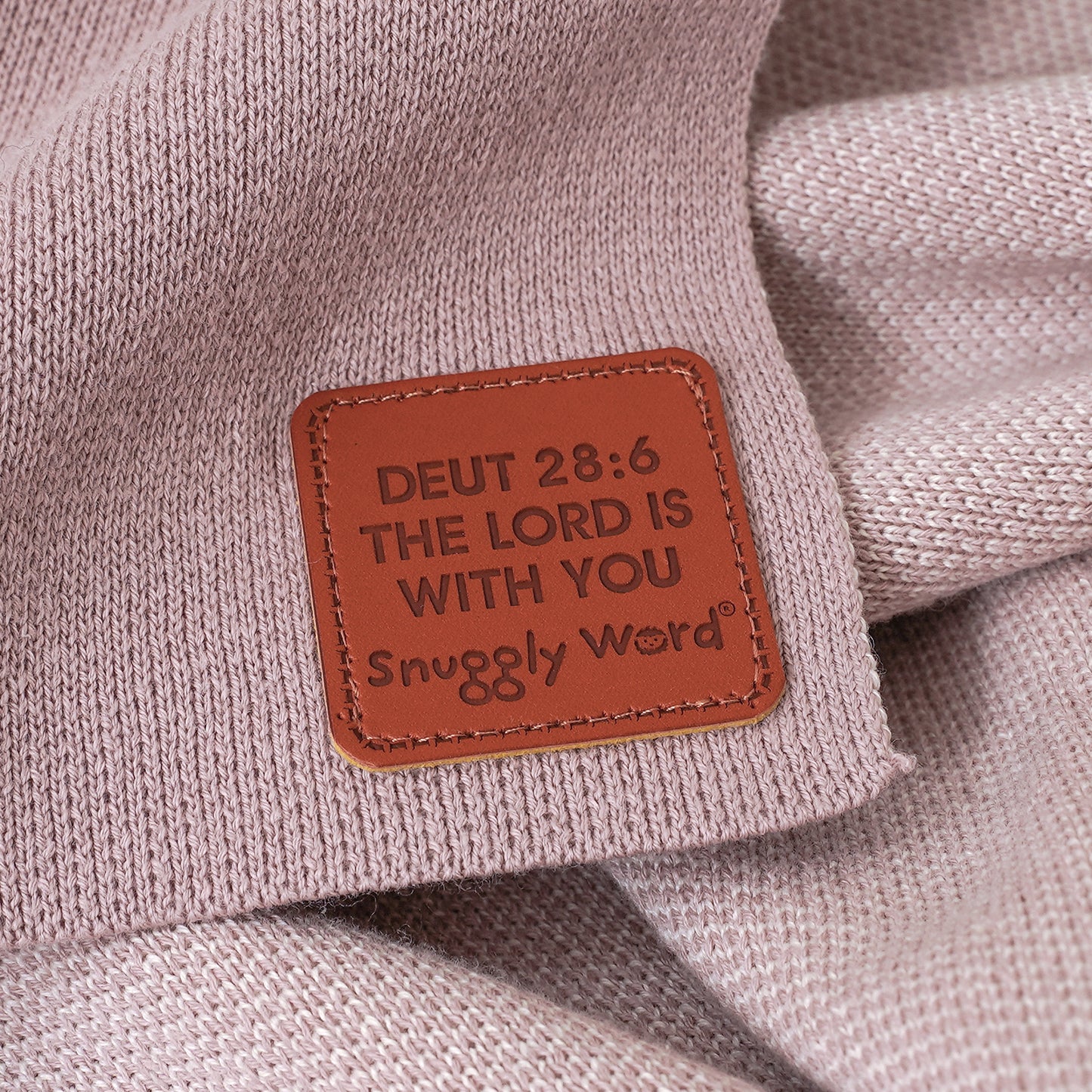 Close-up of a pink Forever Blessed baby blanket with a brown faux leather tag showing Deuteronomy 28:6 scripture.