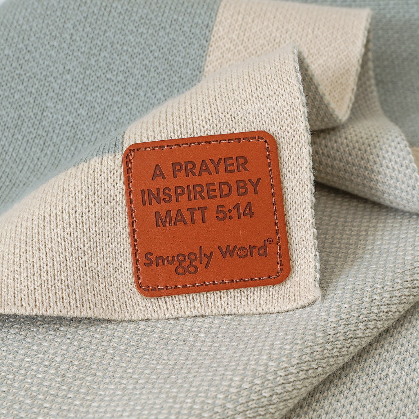 Close-up of a blue and beige Christian baby blanket with "A Prayer Inspired by Matt 5:14" faux leather tag