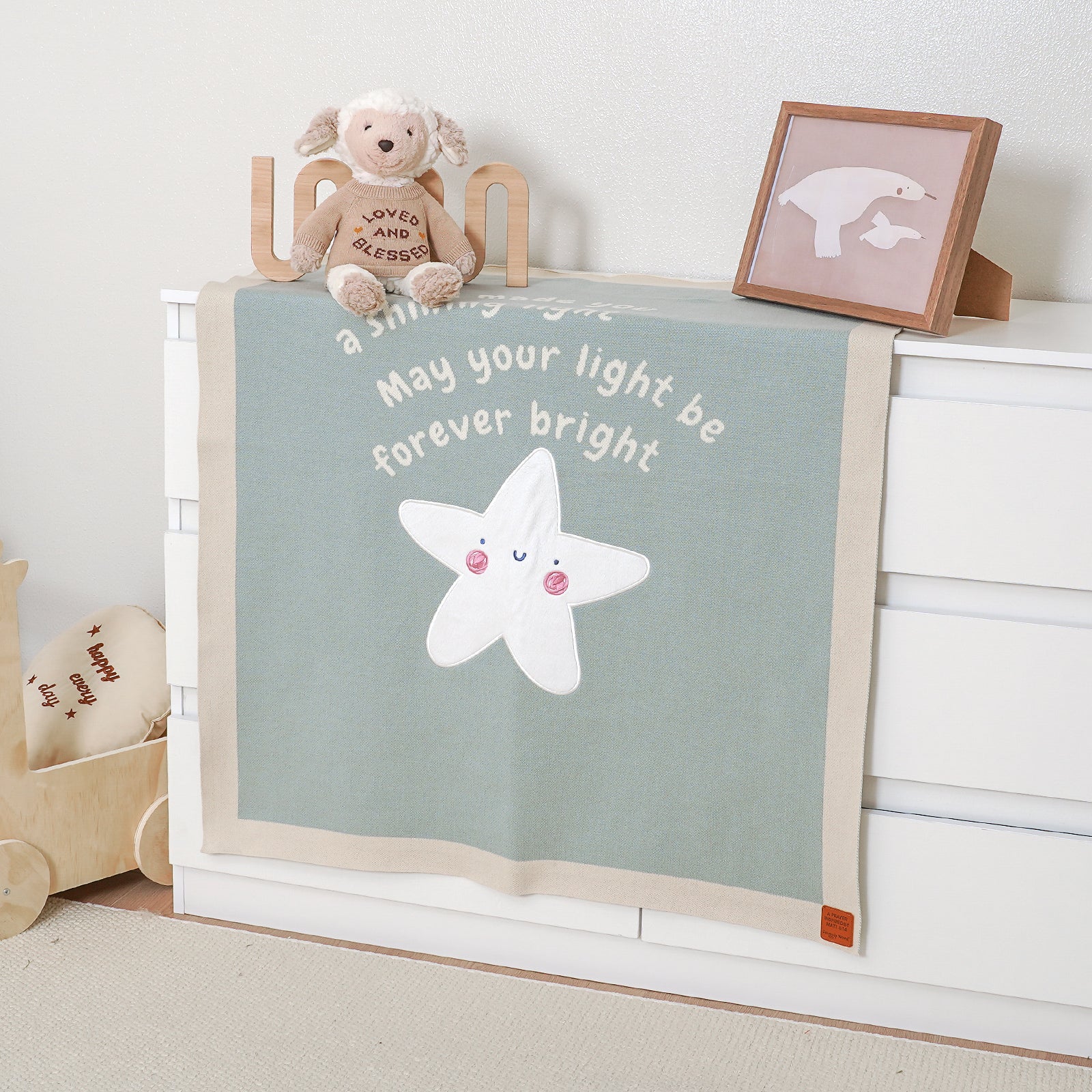 Matthew 5:14 baby blanket with white star and "May your light be forever bright" text on dresser