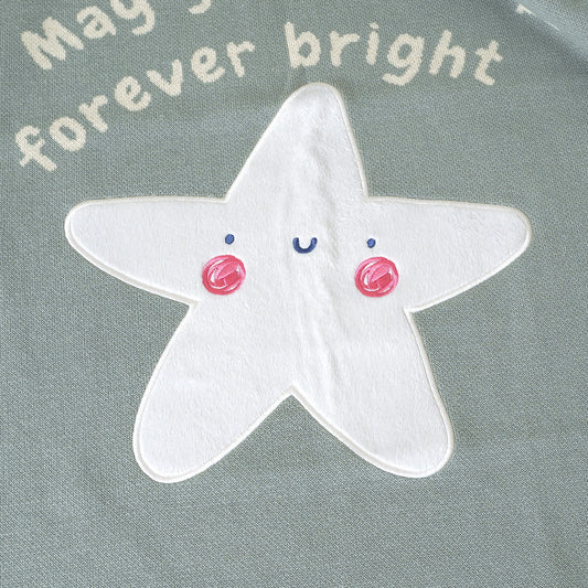 Close-up of 'You Are the Light' baby blanket with plush white star, pink cheeks, blue eyes, 'forever bright' text.