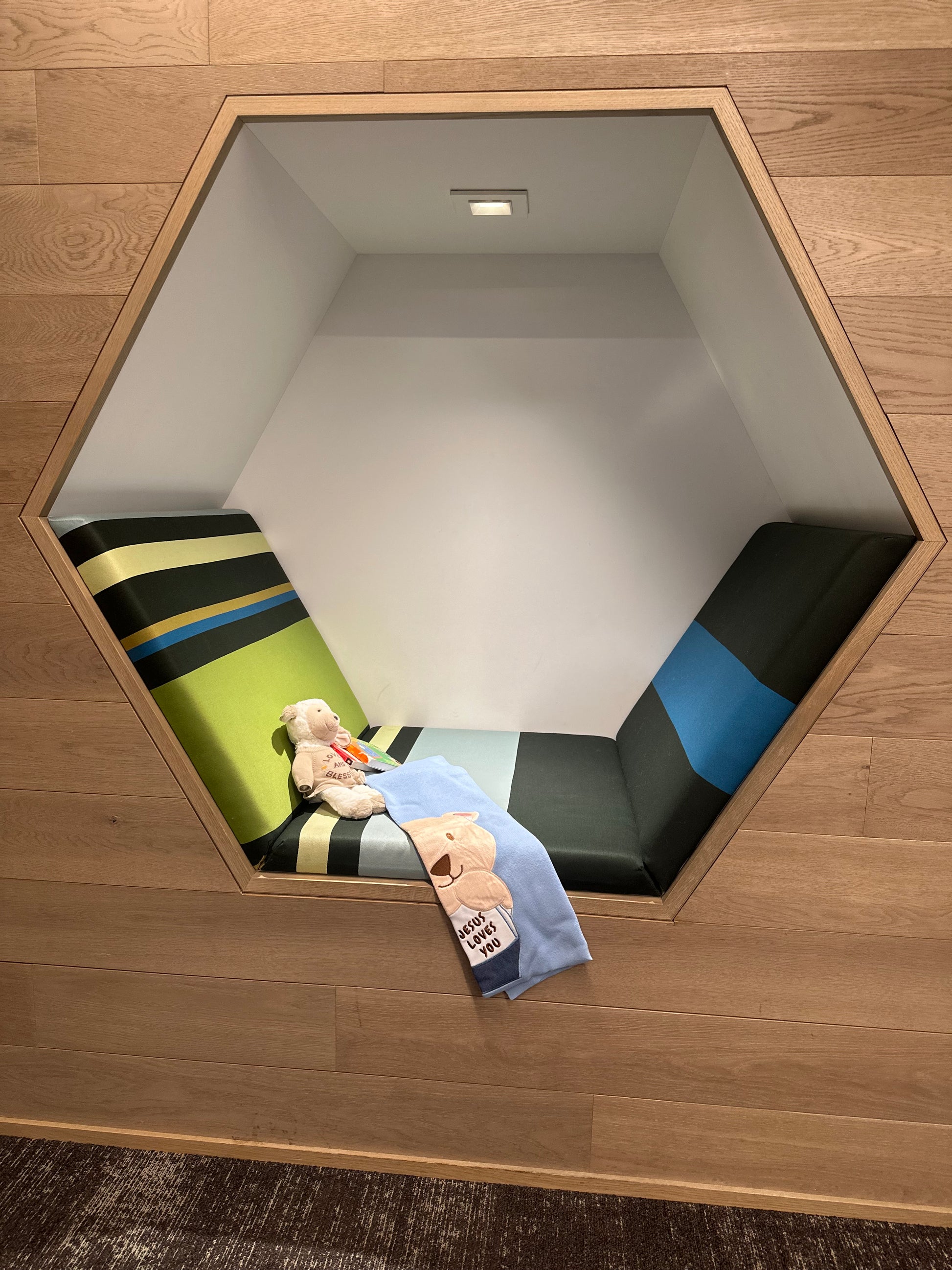 Little Lamb plush toy in a hexagon alcove with colorful striped cushions. Ideal baby nursery decor or keepsake gift.