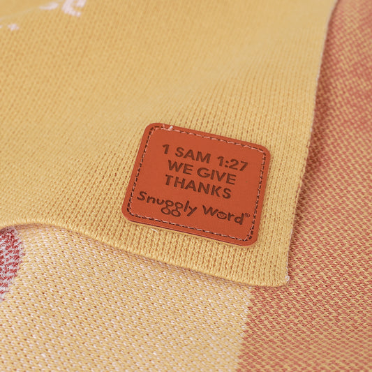 Close-up of Christian baby blanket tag with 1 Samuel 1:27 and "Snuggly Word" on brown faux leather label