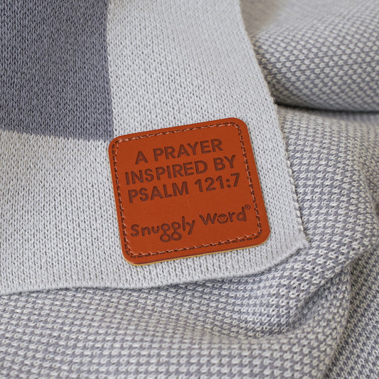 Close-up of brown leather patch on gray and white knitted Watched Over Psalm 121:7 baby blanket with text.