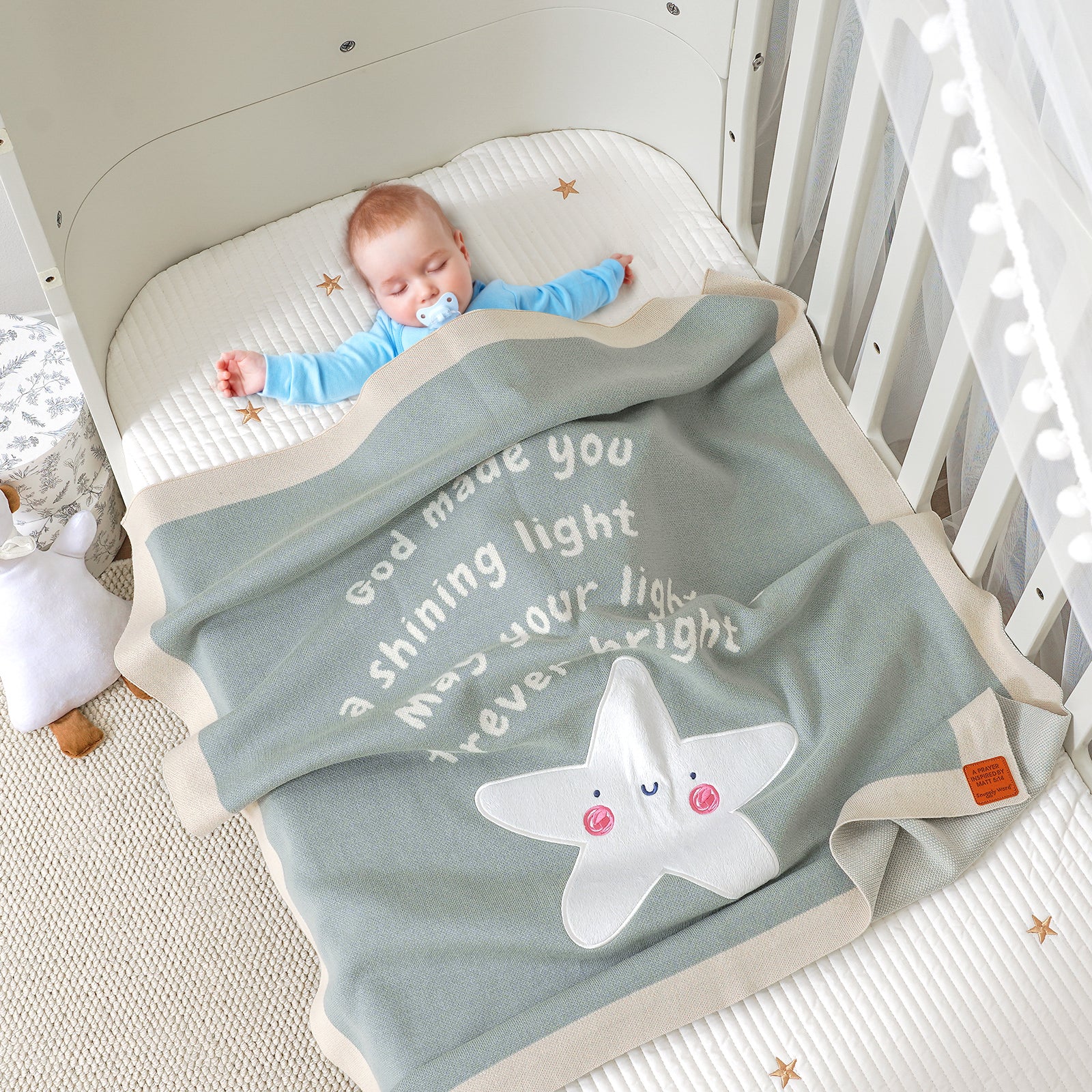 Baby sleeping with pacifier in a crib, covered by a sage green 'You Are the Light' Matthew 5:14 Scripture blanket.