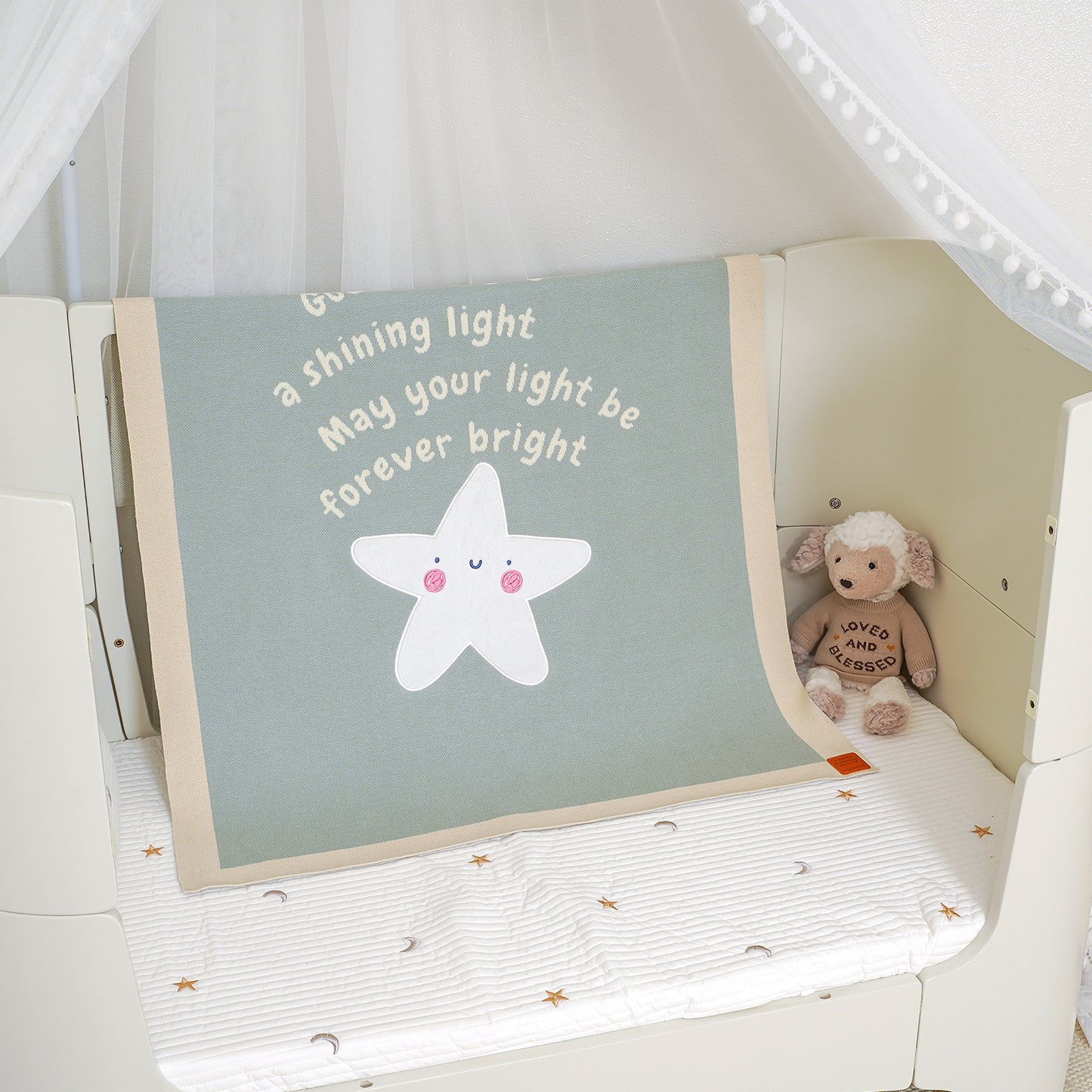 Matthew 5:14 baby blanket with 'You are a shining light' quote & star, draped over a crib with a stuffed animal.